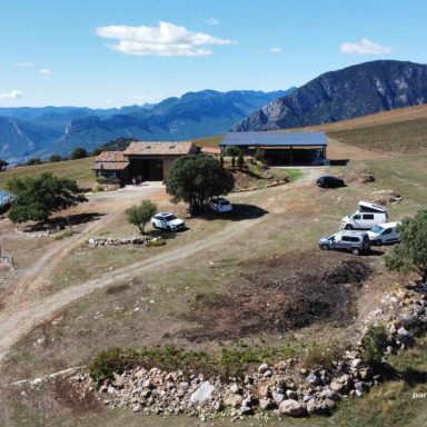 Paisaje montañoso con casas rústicas y vehículos en un camino de tierra.