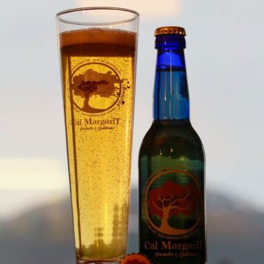 Copa de cerveza amarilla junto a una botella azul con etiqueta de árbol.