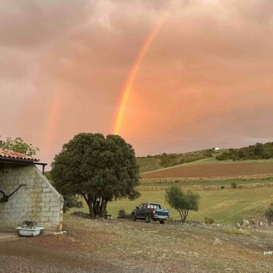 Arcoíris sobre un paisaje rural con una casa y un vehículo en el campo.